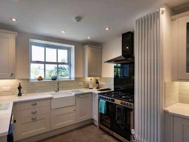 A kitchen with a window above a sink a stove with towels hanging and a tall radiator at Ayr Farmhouse in St Ives