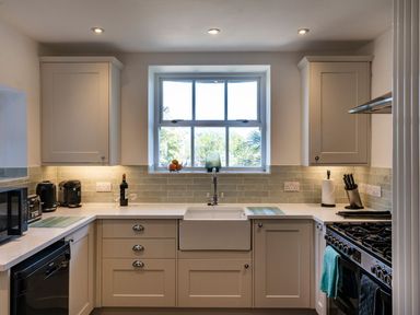 A kitchen with white cabinets a window above the sink and appliances at Ayr Farmhouse in St Ives