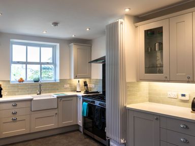 A kitchen with a window above a sink an oven with towels hanging and cabinets at Ayr Farmhouse in St Ives