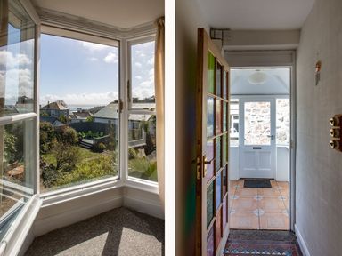 A view of a garden with green chairs through a bay window and a hallway with a door leading outside at Ayr Farmhouse in St Ives