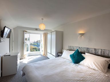 A bedroom with a bed a blue pillow a wardrobe a chest of drawers and a bay window at Ayr Farmhouse in St Ives