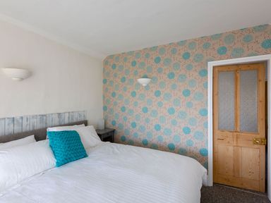 A bedroom with a bed with white linens and a blue pillow a wooden door and a floral wallpaper at Ayr Farmhouse in St Ives