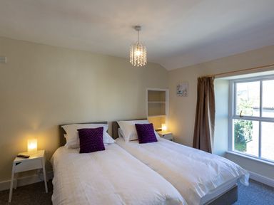 A bedroom with two single beds side by side with white bedding and purple cushions Ayr Farmhouse St Ives
