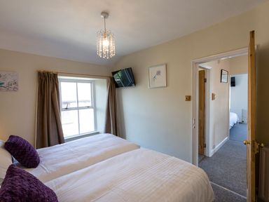 A bedroom with two beds and purple pillows next to a window with curtains at Ayr Farmhouse in St Ives