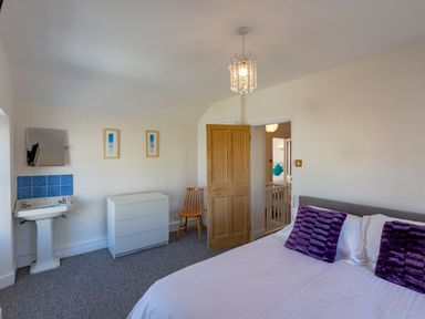 A bedroom with a bed with purple pillows a wooden door a white dresser a wooden chair and a sink at Ayr Farmhouse in St Ives