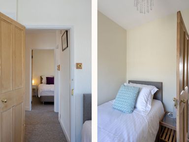 A bedroom with a single bed and blue cushion next to a wooden nightstand and a view through an open door to another bedroom with a double bed at Ayr Farmhouse in St Ives