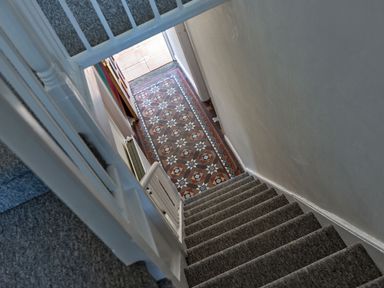 A staircase with grey carpet leading down to a hallway with patterned tile floor at Ayr Farmhouse in St Ives