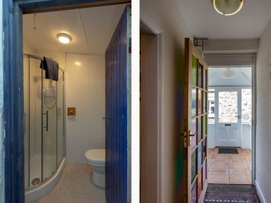 A small bathroom with a shower enclosure and a toilet next to a hallway with a door featuring colorful glass panels at Ayr Farmhouse in St Ives