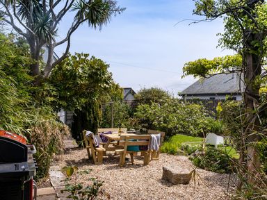 An outdoor garden area with a wooden table and benches surrounded by greenery and a barbecue grill at Ayr Farmhouse in St Ives