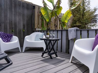 An outdoor patio with white chairs and cushions a small black table with wine glasses and a bottle at Ayr Farmhouse in St Ives