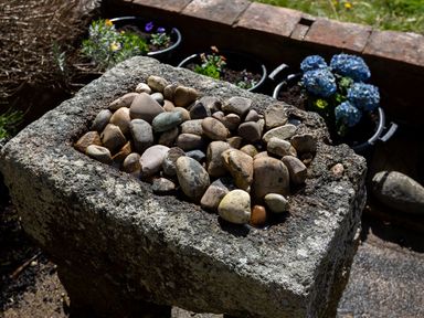 A stone birdbath filled with pebbles with flower pots and a brick wall in the background at Ayr Farmhouse in St Ives