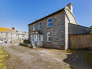 A stone detached house with white-framed windows and a wooden gate on a driveway at Ayr Farmhouse in St Ives