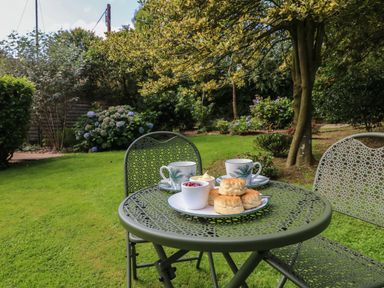A green metal garden table and chairs with scones jam and cups of tea in a garden at Jasmine Bydown near Barnstaple