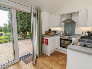 A kitchen with an oven stovetop microwave toaster and sink with drying rack next to a door opening to a patio and garden at Jasmine Bydown near Barnstaple