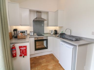 A kitchen with white cabinets wooden floor oven stovetop refrigerator and fire safety equipment at Jasmine Bydown near Barnstaple