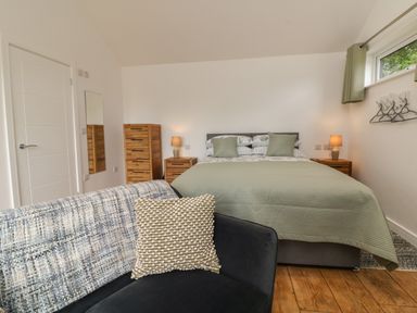 A bedroom with a bed green bedding wooden furniture and a sofa with cushions at Jasmine Bydown near Barnstaple