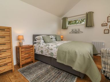 A bedroom with a bed green bedding wooden nightstand and dresser at Jasmine Bydown near Barnstaple