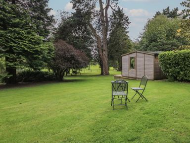 A backyard with metal chairs and a table near a wooden shed surrounded by trees and grass at Jasmine Bydown near Barnstaple