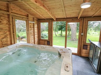 An indoor wooden room with a hot tub and windows overlooking a garden at Jasmine Bydown near Barnstaple