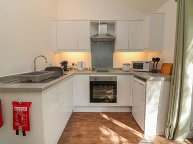 A kitchen with white cabinets a sink an oven a microwave and kitchen utensils at Fern Bydown near Barnstaple