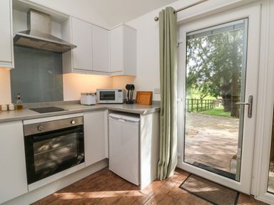 A kitchen with white cabinets an oven a microwave and a glass door leading outside at Fern Bydown near Barnstaple
