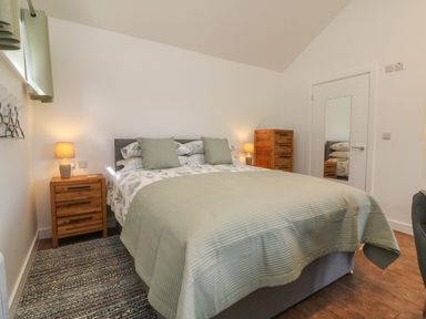 A bedroom with a bed a wooden nightstand with a lamp a chest of drawers and a mirror on the door at Fern Bydown near Barnstaple