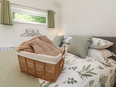 A bedroom with a bed featuring botanical bedding and cushions and a basket with blankets at Fern Bydown near Barnstaple