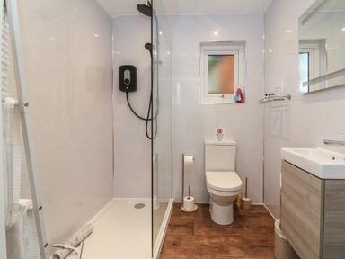 A bathroom with a shower, toilet, sink, and a small window at Fern Bydown near Barnstaple