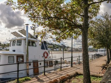 A boat docked by a riverside walkway next to trees and benches at Fern Bydown near Barnstaple