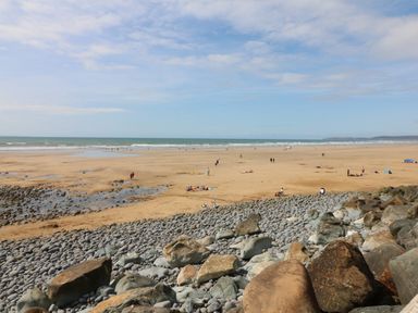 A beach with rocks in the foreground and people on the sand near the ocean at Fern Bydown near Barnstaple