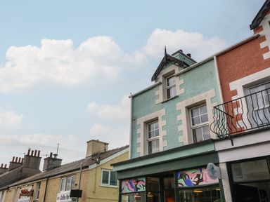 A row of colorful attached buildings with shopfronts and windows under a cloudy sky at The Bell Apartment in Cemaes Bay