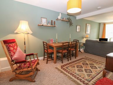 A living room with a rocking chair dining table with chairs wooden shelves and a sofa at The Bell Apartment in Cemaes Bay