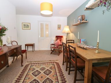 A dining room with a wooden table and chairs a rocking chair a sideboard a patterned rug and wall shelves at The Bell Apartment in Cemaes Bay