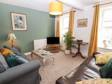 A living room with two sofas a coffee table a television a floor lamp a potted plant and two windows with yellow curtains at The Bell Apartment in Cemaes Bay
