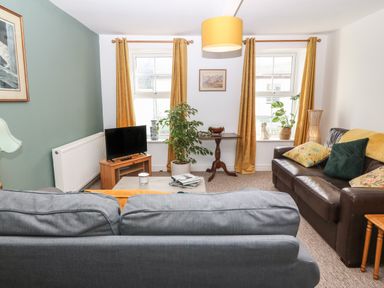A living room with two sofas a television on a wooden stand a coffee table and yellow curtains at The Bell Apartment in Cemaes Bay