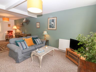 A living room with a sofa a coffee table a TV on a stand and a dining table in the background at The Bell Apartment in Cemaes Bay