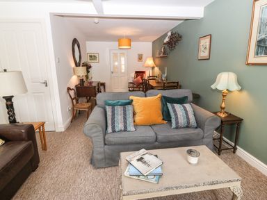 A living room with a gray sofa and cushions a coffee table with books and a candle lamps and a dining table at The Bell Apartment in Cemaes Bay