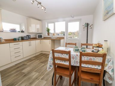 A kitchen with wooden chairs and a table covered with a leaf patterned cloth at The Bell Apartment in Cemaes Bay