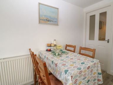 A dining room with a table covered in a patterned tablecloth and wooden chairs at The Bell Apartment in Cemaes Bay