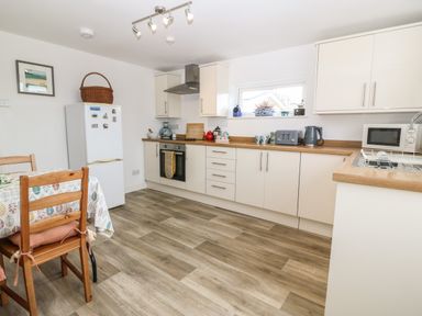 A kitchen with white cabinets wooden countertops a dining table with chairs a refrigerator and various kitchen appliances at The Bell Apartment in Cemaes Bay