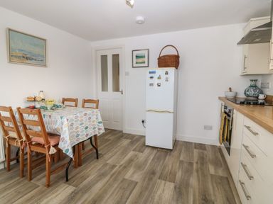 A kitchen with a dining table and wooden chairs a white refrigerator and kitchen cabinets at The Bell Apartment in Cemaes Bay