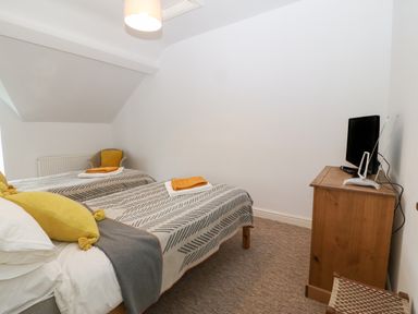 A bedroom with two single beds a wooden dresser with a television and a chair at The Bell Apartment in Cemaes Bay