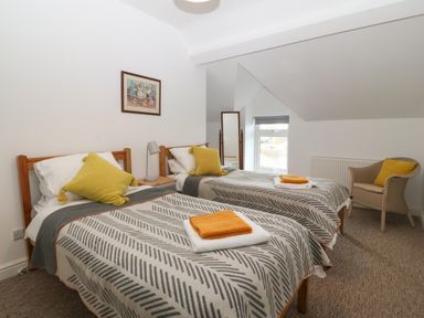 A bedroom with two single beds with patterned blankets and yellow pillows and a chair with a yellow pillow at The Bell Apartment in Cemaes Bay