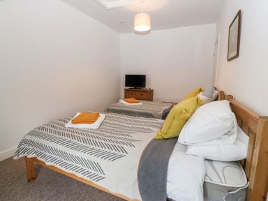 A bedroom with two single beds nightstand with a television and a wall painting at The Bell Apartment in Cemaes Bay