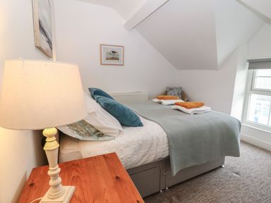 A bedroom with a bed covered in blue and white bedding a wooden bedside table with a lamp and a window at The Bell Apartment in Cemaes Bay