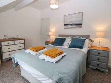 A bedroom with a double bed two bedside tables with lamps a chest of drawers and a painting above the bed at The Bell Apartment in Cemaes Bay
