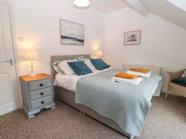A bedroom with a bed with blue pillows and folded towels bedside tables with lamps and framed pictures on walls at The Bell Apartment in Cemaes Bay
