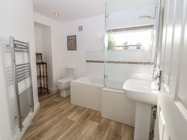 A bathroom with a toilet bathtub sink towel rack and wooden floor at The Bell Apartment in Cemaes Bay