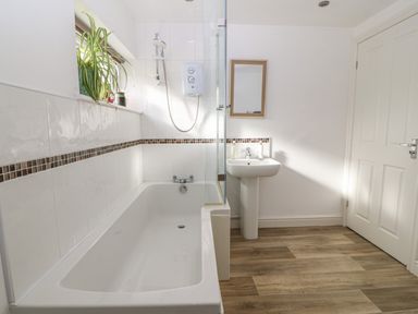 A bathroom with a bathtub shower combination a sink with a mirror and a plant on the windowsill at The Bell Apartment in Cemaes Bay