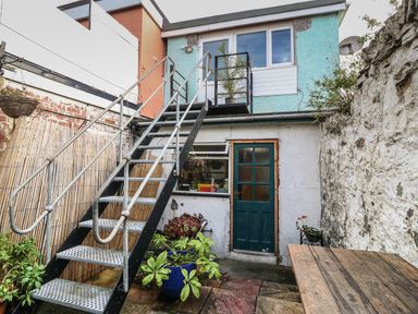 A small outdoor area with metal stairs leading to a second floor door a wooden table and potted plants at The Bell Apartment in Cemaes Bay